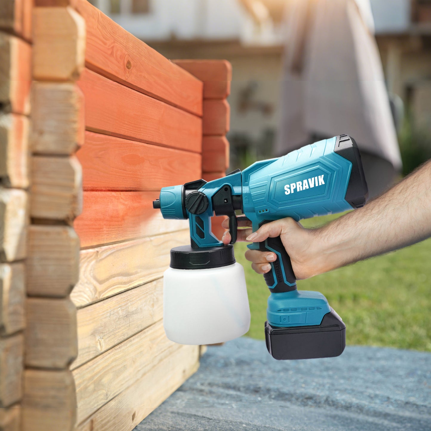 Person using a Spravik paint sprayer to paint wooden planks outdoors.