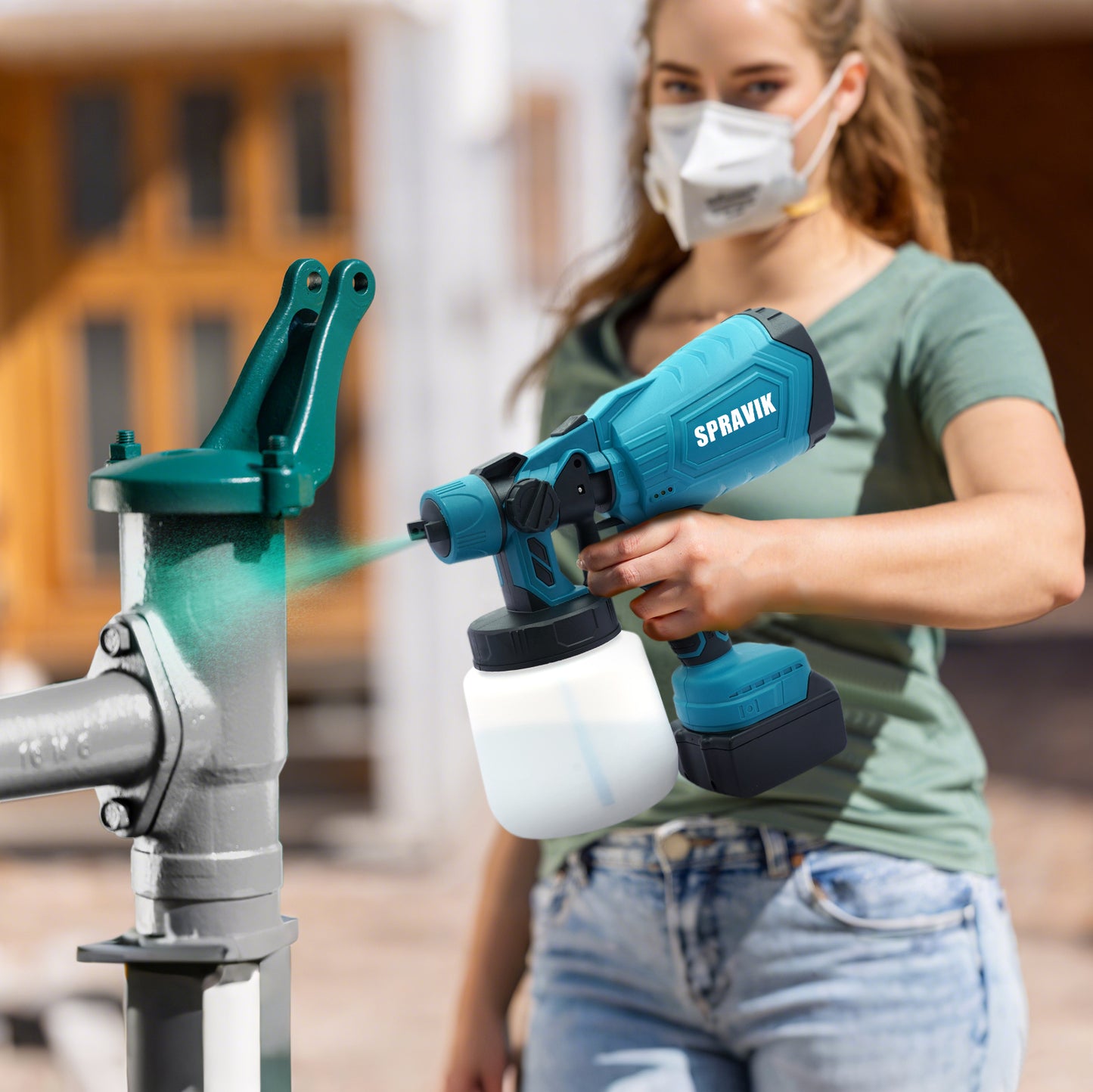 Person using a Spravik paint sprayer on a metal surface outdoors.