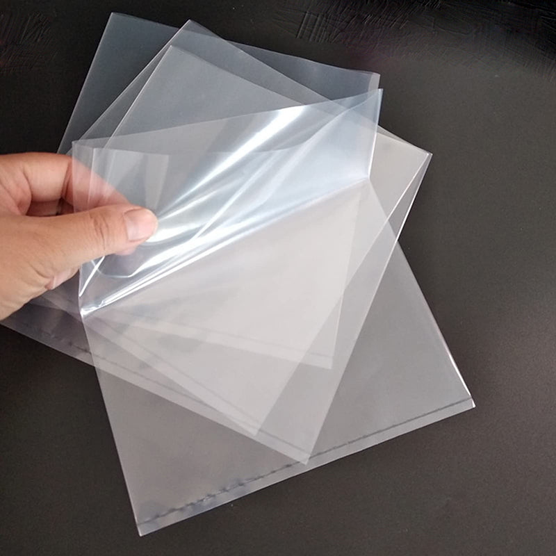 Hand holding clear plastic sheets on a dark surface